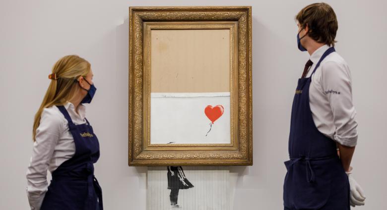 Two Sotheby's employees stand, framing the Banksy piece on auction day Oct 14, 2021