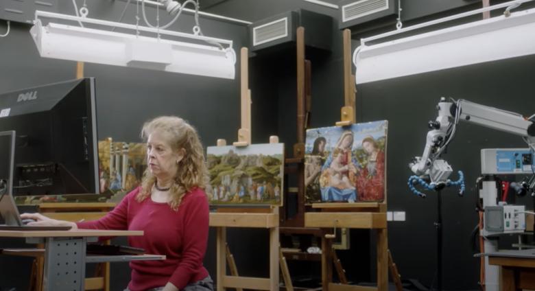 conservator looks at computer in front of several paintings