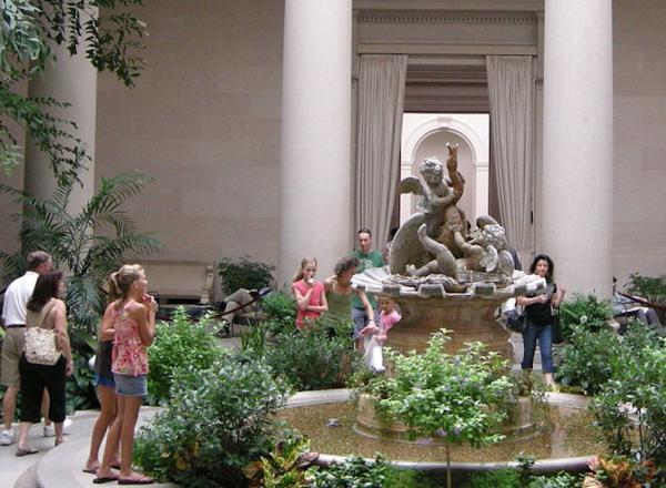 Family with children mill around the interior gardens of the West Building.